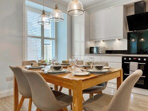 A modern kitchen with a dining table set for four, equipped with a microwave, stove, and oven. - 3 bedroom accommodation in Eyemouth (Eyemouth)