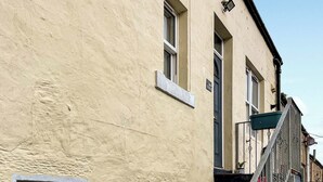 Een gebouw met een structuurrijk beige uiterlijk, een trap die leidt naar een balkon met een metalen hekwerk, en een klein raam met een gesloten luik.