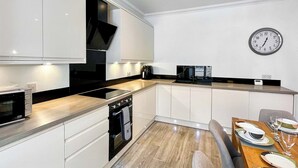 Een moderne keuken met witte kasten, een ingebouwde oven, een magnetron en een eethoek met een houten tafel en stoelen.