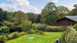 Ein gepflegter Garten mit Rasen, einem runden, blauen Spielbereich und einem Holzgebäude mit Schrägdach.