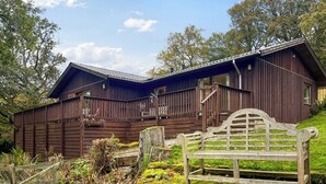 Ein hölzernes Bauernhaus mit Balkon, umgeben von Bäumen und einer Rasenfläche.