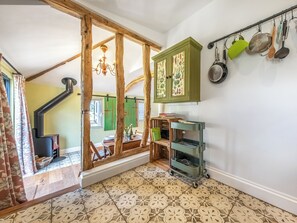 A rustic interior with exposed wooden beams, a green cabinet with fruit patterns, a hanging pot rack, and a tiled floor. - The Old Press - UK50806 (Cratfield, near Laxfield)