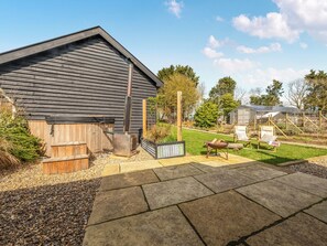 A rustic wooden building with a chimney, a gravel area, and a garden with a wooden bench and a table. - The Old Press - UK50806 (Cratfield, near Laxfield)