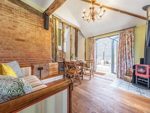 Een rustieke kamer met zichtbare bakstenen muren, een houten bank, een eettafel met stoelen, een kroonluchter en een houtkachel.