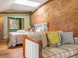 A room with a brick wall, a wooden ceiling, a bed with a striped mattress, a wooden chair, and a small table with a vase of flowers. - The Old Press - UK50806 (Cratfield, near Laxfield)