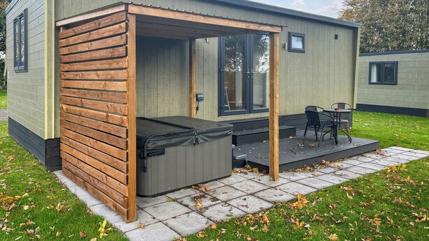 A modern, compact mobile home with a patio area featuring a hot tub, outdoor seating, and a small table.