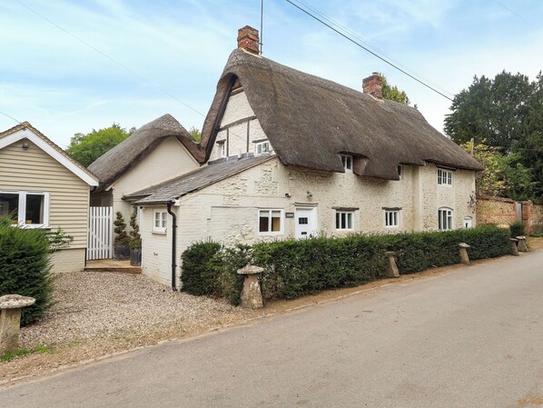 A traditional thatched-roof house with a white exterior, a gravel driveway, and a hedge in front.