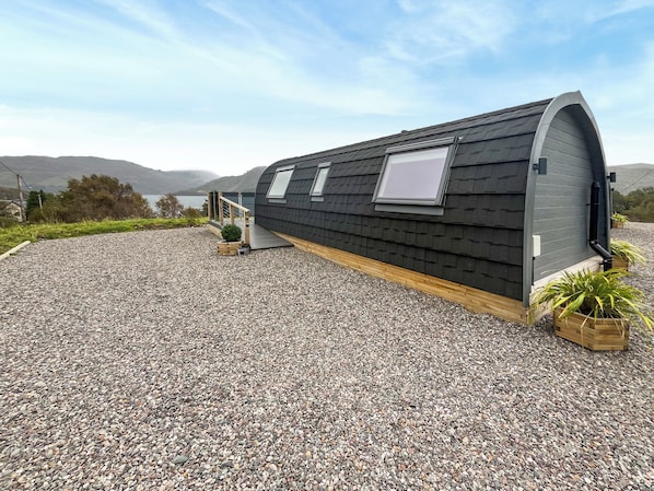 A modern, curved-roofed building with a gravel driveway and potted plants.