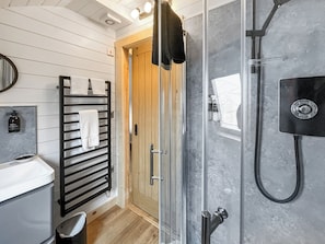 A modern bathroom with a glass shower enclosure, a black towel rack with white towels, a wooden door, and a white sink.