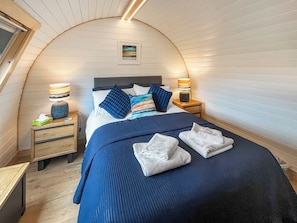 A bedroom with a curved ceiling, a bed with blue bedding, two bedside tables with lamps, and a small picture on the wall.