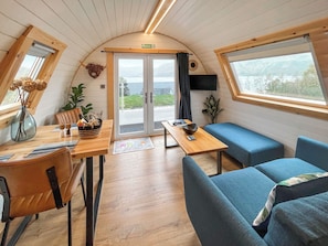 A cozy interior with a wooden table, blue seating, a TV, and a view through the glass doors.