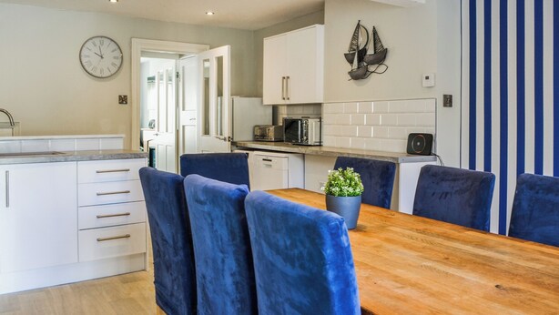 A modern kitchen with white cabinets, a wooden dining table, and blue chairs. - 4 bedroom accommodation in Filey (Filey)