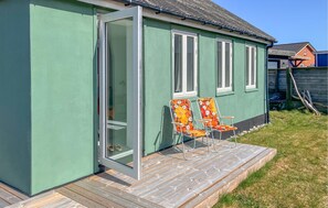 A green house with a wooden deck, two chairs with floral upholstery, and a sliding glass door. - Lovely home in Thyborøn with WiFi (Thyborøn)