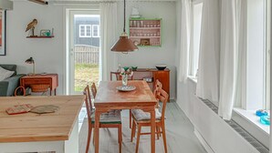 Een eetruimte met een houten tafel en stoelen, een vaas met bloemen en een hanglamp.