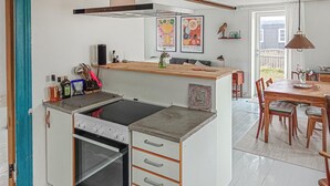 Een compacte keuken met een inbouwfornuis, oven en opbergladen. Er is een eethoek met een houten tafel en stoelen.