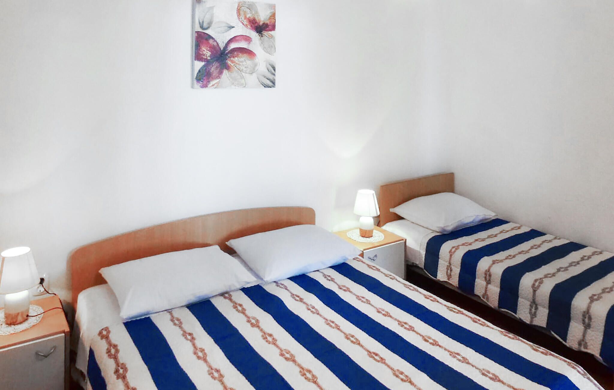 Ein Hotelzimmer mit zwei Betten, jeweils mit einer gestreiften Bettdecke, einem Nachttisch mit einer Lampe und einem an der Wand hängenden Kunstwerk.