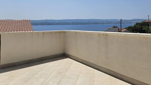 Un coin de balcon avec un sol carrelé, un mur sobre et une vue sur une étendue d’eau et des collines lointaines.