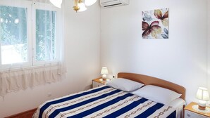 Une chambre d’hôtel comprenant un lit, deux tables de chevet avec des lampes, une fenêtre avec des rideaux, un appareil de climatisation et une œuvre d’art florale accrochée au mur.