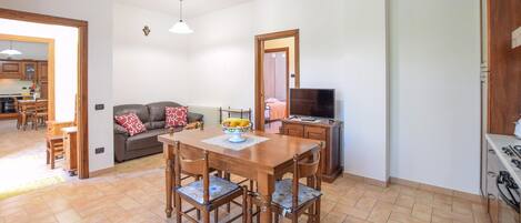 Un comedor con una mesa y sillas de madera, un televisor y una cocina visible al fondo.