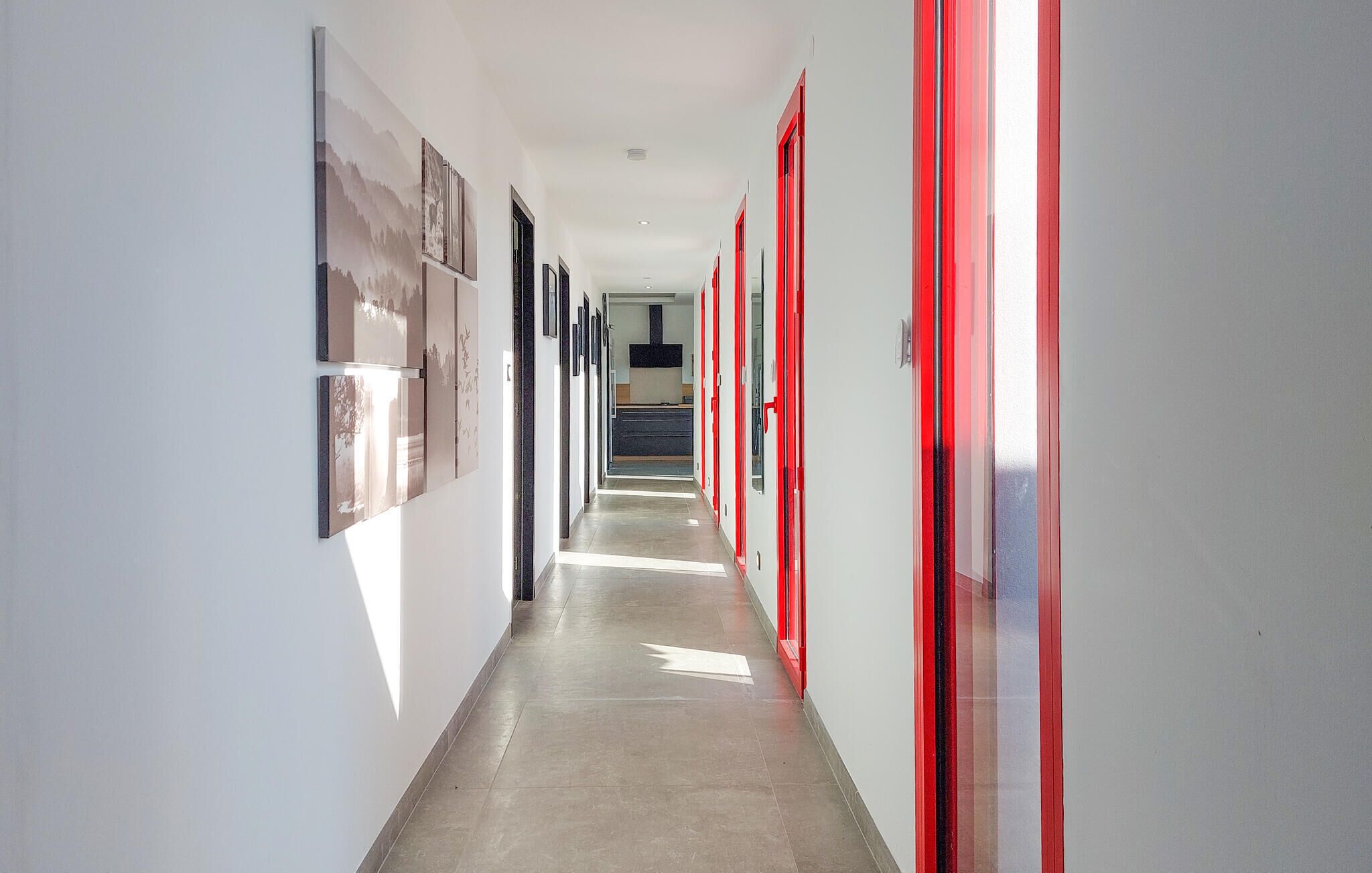 Un couloir avec des portes à encadrement rouge, un sol carrelé et des œuvres d’art accrochées aux murs.