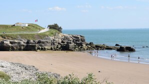 A coastal beach with rocky cliffs, a grassy hill with a flag, and a clear view of the sea. - Villa piscine intérieure (Royan)