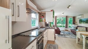A modern kitchen with a central island, a dining area with a sofa and table, and a view of greenery through large windows. - Beautiful home in Voorthuizen (Voorthuizen)