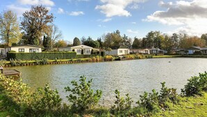 A lakeside view with several houses along the shore, a dock, and a row of trees in the background. - Beautiful home in Voorthuizen (Voorthuizen)