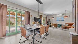 Een ruime woonkamer met een eettafel, comfortabele zithoek, een flatscreen-televisie en een schilderij aan de muur.