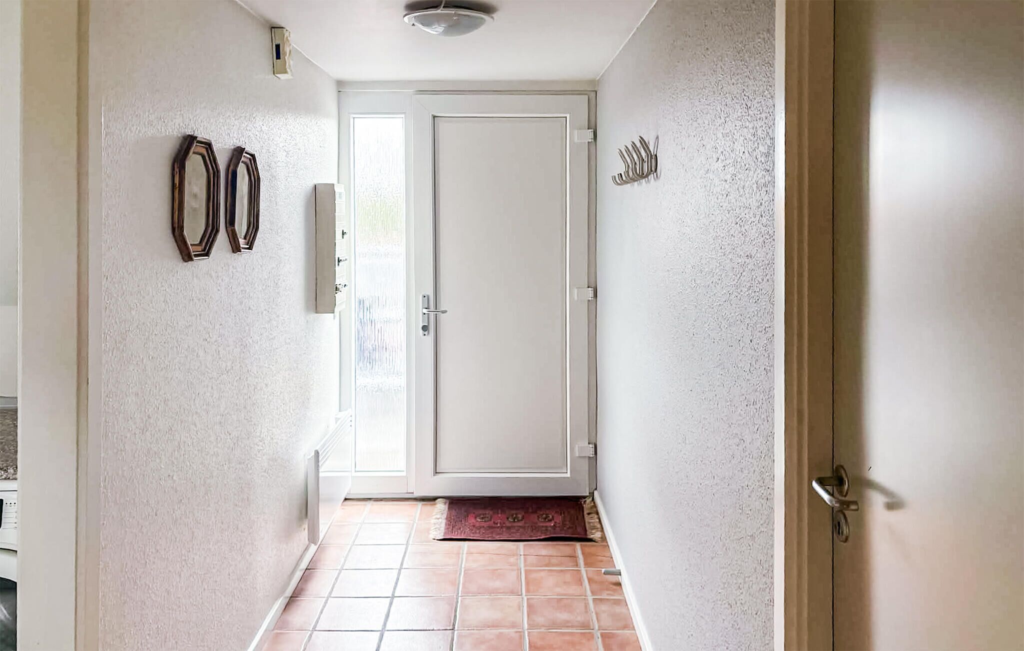 Passadís amb una porta blanca, un paviment de rajoles i una catifa petita.