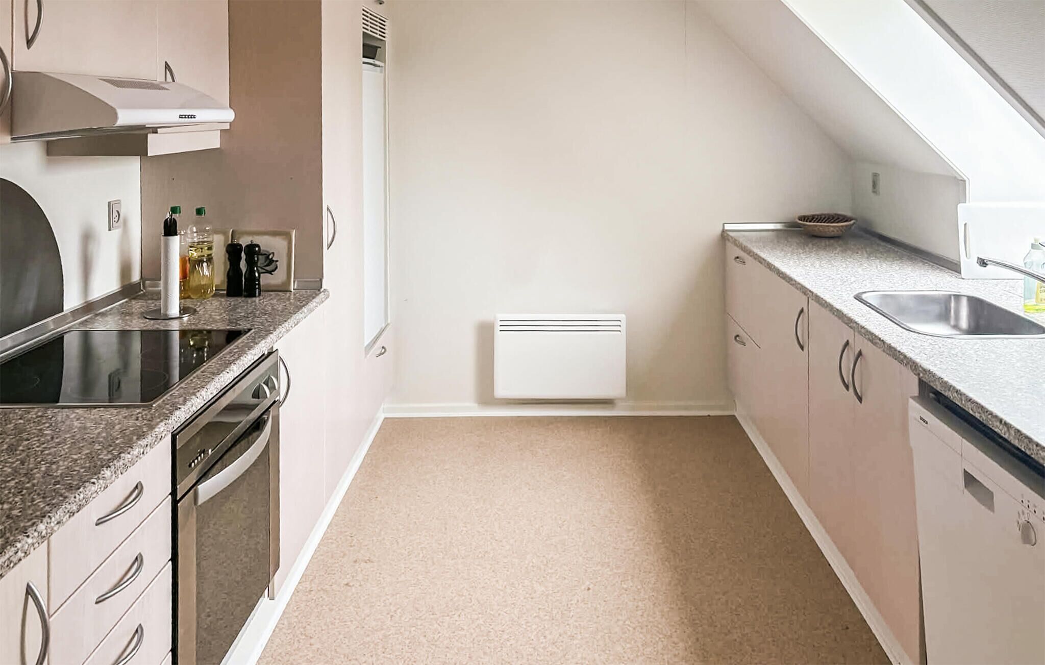 A modern kitchen with a built-in oven, a dishwasher, a sink, and a white wall-mounted heater.