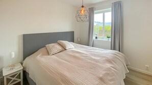 A neatly made bed with a geometric-patterned headboard, a bedside table with a lamp, and a window with curtains.