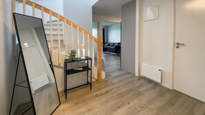 A hallway with a wooden staircase, a black console table with a plant, and a white door.