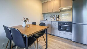 A modern kitchen with a wooden dining table, black chairs, a built-in oven, and a stainless steel refrigerator.