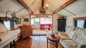 A cozy loft-style living room with wooden floors, a red sofa, a patterned armchair, and a small table. - Lake front home in Leksand with lake view (Leksand)