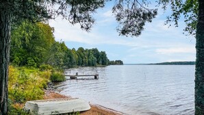 A lakeside view with a dock extending into calm waters, surrounded by dense greenery and trees. - Lake front home in Leksand with lake view (Leksand)