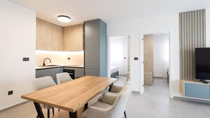 A modern kitchen with wooden cabinets, a dining area with a wooden table and white chairs, and a living area with a flat-screen TV. - Nice apartment in Privlaka with WiFi (Privlaka)