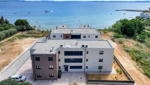 A modern multi-story building with a flat roof, large windows, and a parking area in front. - Nice apartment in Privlaka with WiFi (Privlaka)