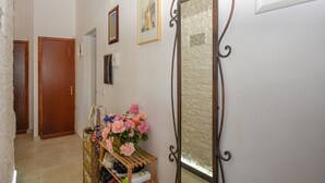Un couloir avec une porte en bois, un miroir et un porte-chaussures contenant des chaussures et des fleurs.