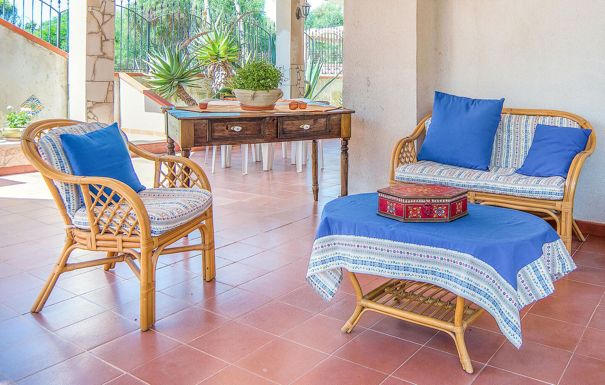 A room with wicker furniture, a patterned tablecloth, and a potted plant.