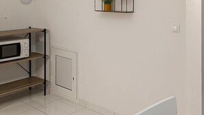 Een keuken met een magnetron op een plank, een klein kastje en een plant in een pot op een wandplank.