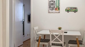 Een kamer met een witte tafel en stoelen, een klein plantje op de tafel, en een wanddecoratie met een auto en tekst.