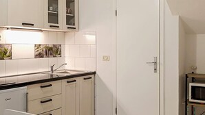 Een moderne keuken met witte kasten, een zwart aanrecht en een spoelbak. Boven het aanrecht bevinden zich kasten met glazen deuren, en er is een magnetron in de hoek zichtbaar.