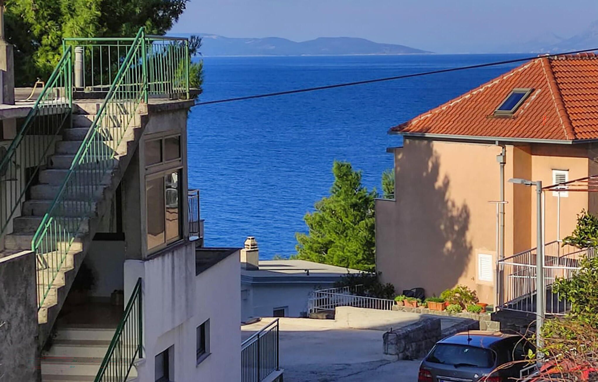Un bâtiment situé sur la côte, doté d’un escalier, avec une voiture garée devant et une vue sur la mer.