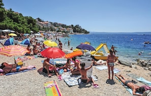 Ein überfüllter Strand mit badenden Personen, Sonnenschirmen und Booten.