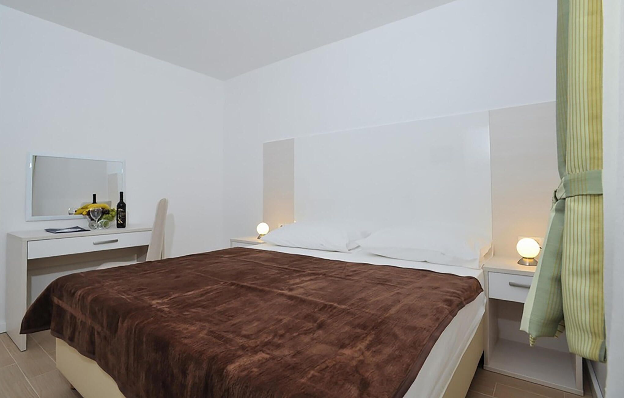 Een slaapkamer met een bed, nachtkastje, kaptafel, spiegel en lamp.