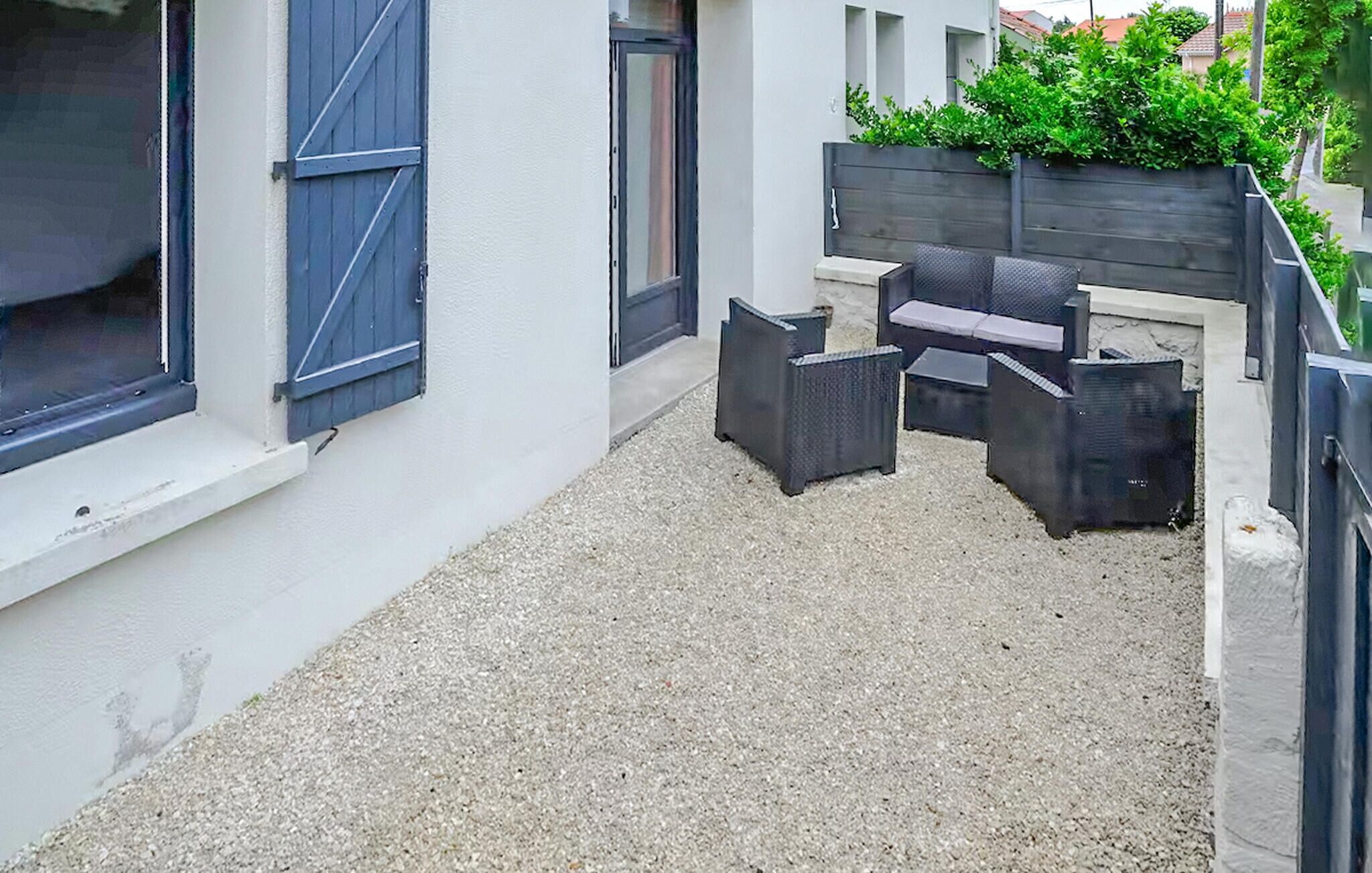 A small outdoor patio area with a gravel floor, a dark-colored sofa set, and a wooden planter with greenery.