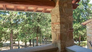Puinen pergola, jonka alla on kivipilari ja josta avautuu näkymä puihin.