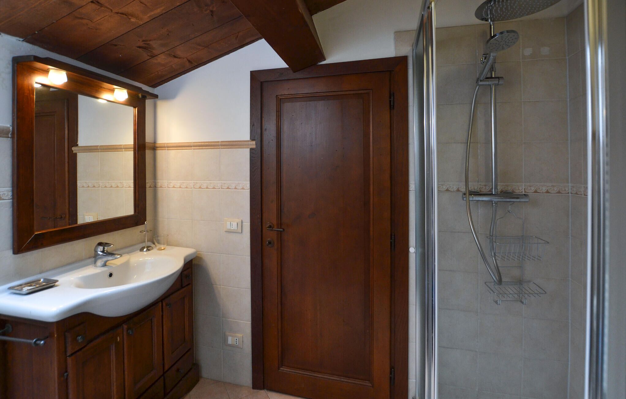 Ein Badezimmer mit Holztür, Waschbecken mit Spiegel und Duschkabine aus Glas.