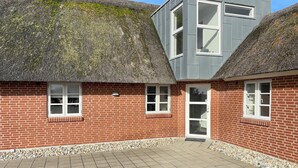 Une maison avec un toit de chaume et une extension moderne dotée de grandes fenêtres.