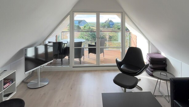 Un espace de vie moderne à aire ouverte, doté d’une grande porte vitrée donnant sur une terrasse extérieure.